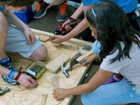 Girl using a hammer and another student using a drill