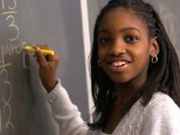 Young African American girl smiling holding chalk in front of a black board