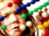A young girl is intently looking at a wooden Abacus counting number frame, moving the colorful balls along the wire frames. 