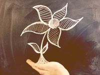 Someone's hand is beneath a chalkboard drawing of a flower, making it look like they're holding the flower in their palm.