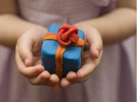 A closeup of a young kid's hands cupping a blue Play-Doh boxed gift with orange Play-Doh ribbon and a red Play-Doh bow.
