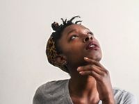 A closeup of a young teenage girl looking up with her head tilt back and her hand under her chin.
