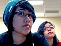 A closeup of two female teens from the shoulder up sitting, looking towards the front of the class.