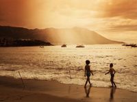 Two young boys in shorts are standing on a beach shoreline.