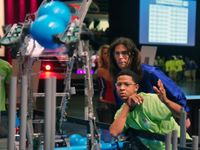 A student and teacher are wearing protective eyewear in an auditorium, looking at a robot.