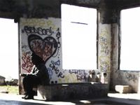 A man is sitting in an abandoned building with graffiti on the cement walls and benches.