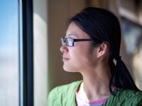 A side shot of a young female teacher in glasses and a green shirt looking out of a window. 