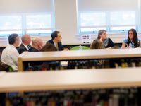 Nine adults are sitting around a table in a library, talking.