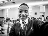 A young boy in a white collared shirt, tie, and sweater is smiling directly into the camera.