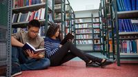 Two high school students reading books in library