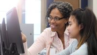 A teacher helps a student working at a computer