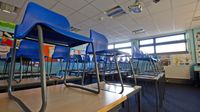 Empty blue chairs stacked on desks in a classroom