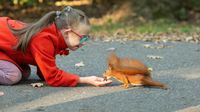 Elementary-aged girl with down syndrome crouches down to feed a squirrel outside