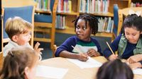 Elementary students talking and working together in a small group at a table