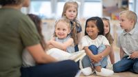 Preschool children listen while teacher reads a book