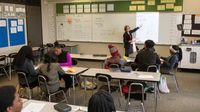 High school math teacher instructs her class in front of a whiteboard