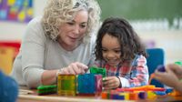 Preschool teacher plays with blocks with student