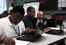 High School students are working on their computers. A teacher is helping them.