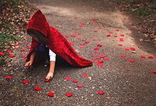 Young girl in a red velvet hooded cape, picking flower petals off the ground