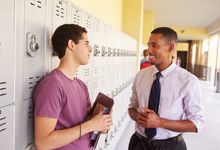 High school teacher talks to a student in the hallway. Both are smiling.