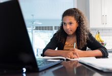 十几岁的女孩在家里参加远程学习课与她的笔记本电脑