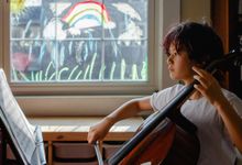 Pre-teen boy practicing cello at home with rainbow painted on window