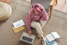 十几岁的女孩坐在家里的地板上用笔记本电脑和书做作业