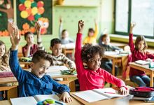 Elementary school students in classroom with hands raised