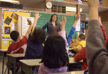 Teacher standing in front of class with students' hands raised