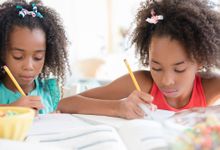 Two girls work on their homework side by side.