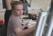 一个十几岁的女孩坐在美术课上，手里拿着一支长长的画笔，在画布上画画。