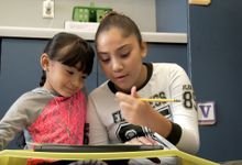 A photograph of an older student working with a younger student.