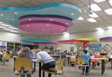 年轻学生在一个大型多功能室的桌子上工作，其中大型彩色装饰悬挂在天花板上。