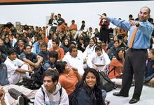 Principal with arms raised talking to a gym full of kids sitting on the floor