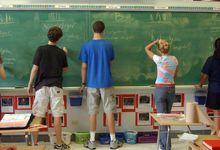 High school students writing Spanish words on chalk board in school. 