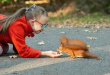 Elementary-aged girl with down syndrome crouches down to feed a squirrel outside