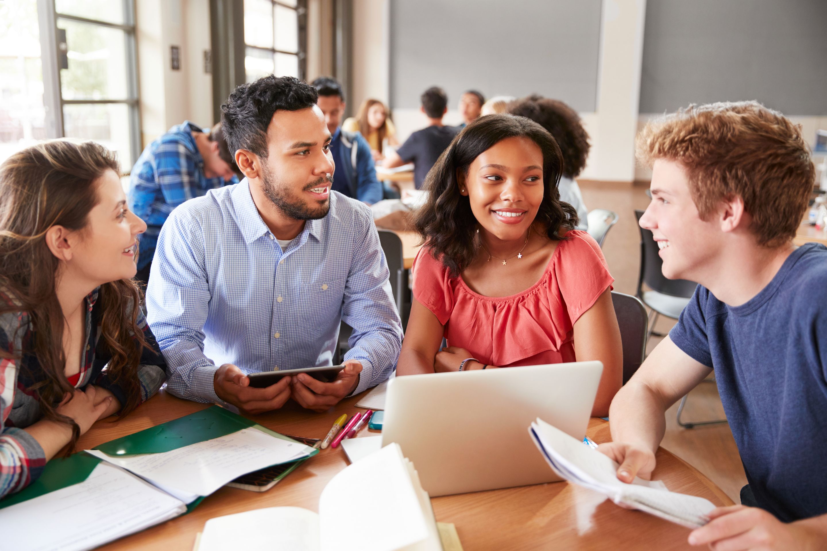  A group of students sitting around a table in a classroom talking to their teacher.