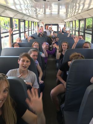 Students on a school bus, all waving and smiling at the camera