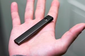 A hand holds a JUUL vaping device.