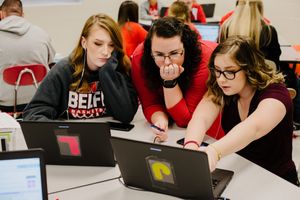 A teacher helping her students with a coding project on their laptops