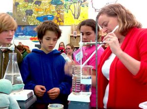 Teacher stirring a liquid in a beaker on a Bunsen burner with three students looking on