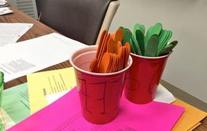 Orange and green popsicle sticks in red plastic cups on a teacher's desk