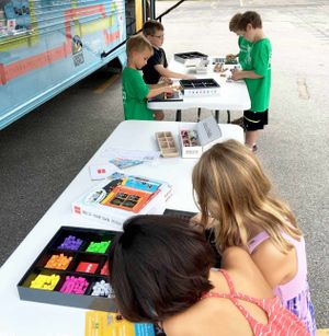 Young kids are making things with electronic building blocks at two pop-up tables beside a bus.