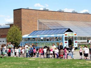 Students line up beside a blue bus with a glass roof. 