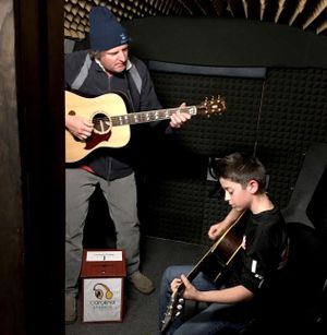 A man and a teenage boy are recording themselves playing guitar inside of a bus.