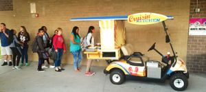 Students are lined up behind a golf cart filled with food that says, "Cruisin' Kitchen."