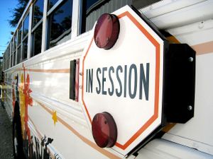 An exterior side shot of a bus. The stop sign says, "In Session," instead of "Stop."