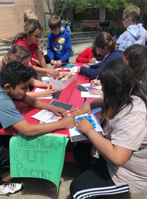 Students at an outdoor picnic table black out words on pages and create poems with the remaining words.