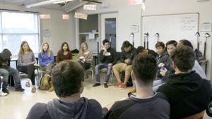 High school students are sitting in chairs, forming a large circle, having a classwide discussion.