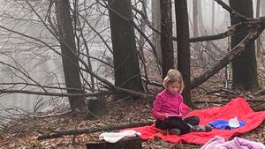 Elementary student sitting on a blanket in the woods reading